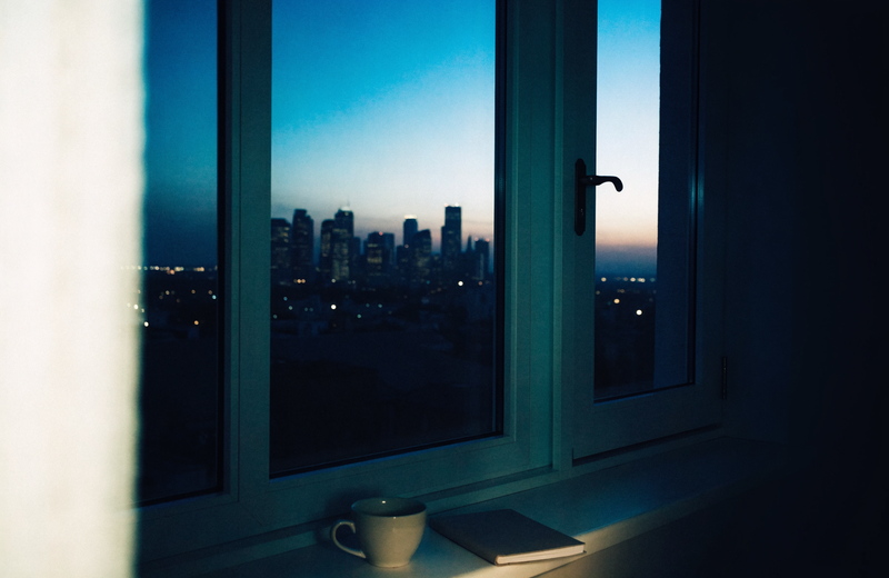 Quiet city skyline at blue hour before dawn seen from a windowsill with a cup and notebook