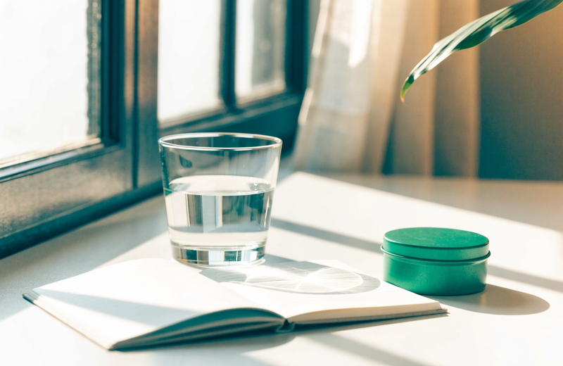 Morning desk with notebook, water and a green mint tin in golden light
