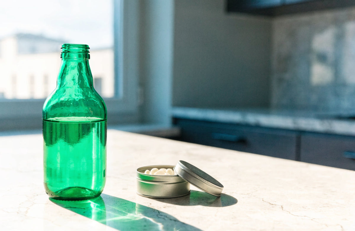 Green shot bottle beside an open mint tin on a kitchen counter