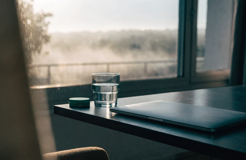 Morning fog clearing outside a window behind a tidy desk with a glass of water and a green mint tin