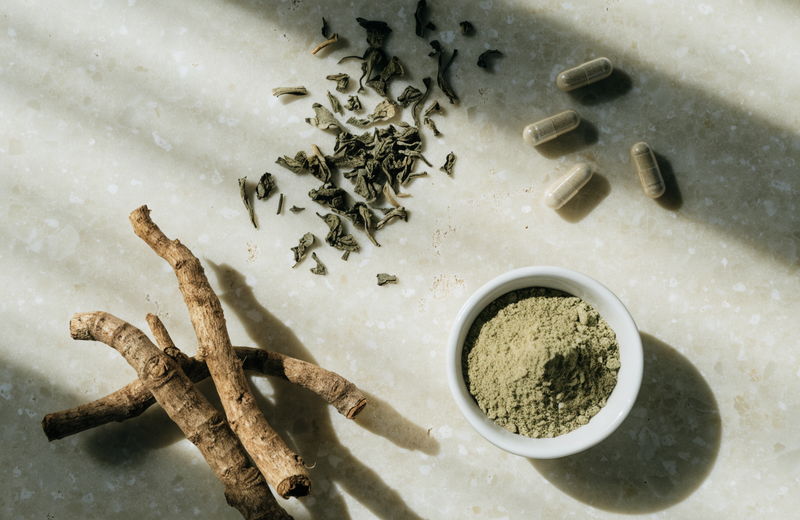 Ashwagandha root, green tea leaves and magnesium capsules arranged on cream stone in soft morning light