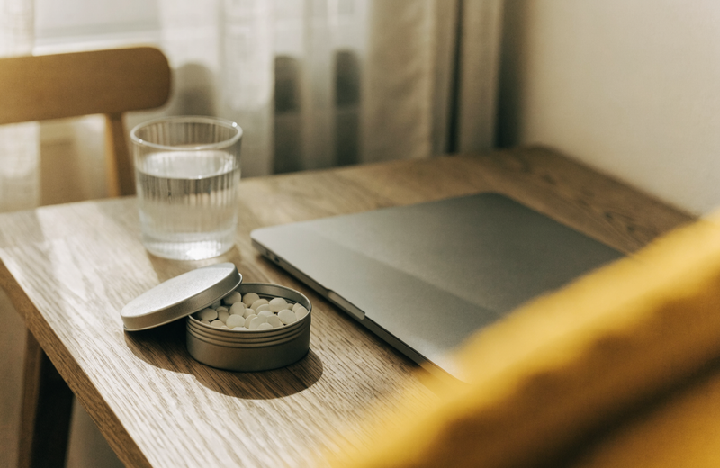 Open tin of white mints on a desk beside a laptop and a glass of water