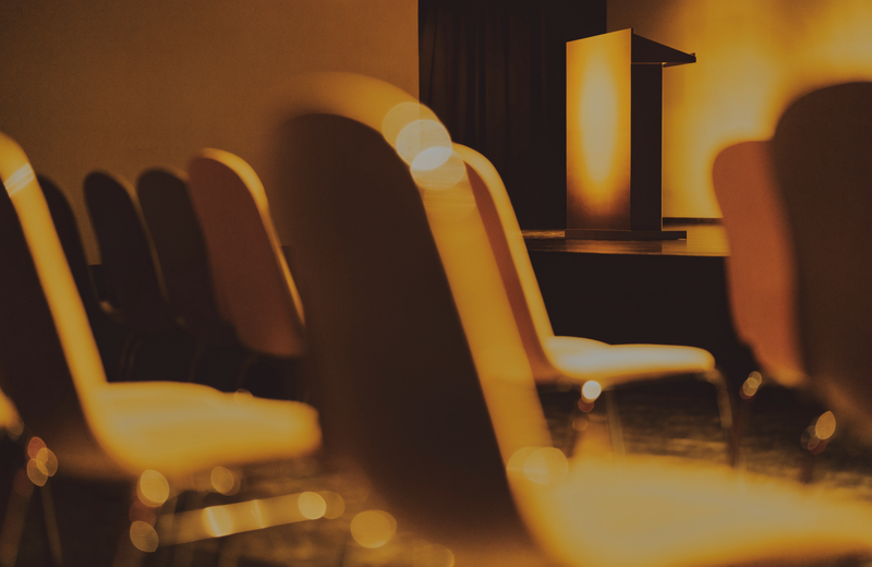 An empty conference stage podium under a warm spotlight before a presentation