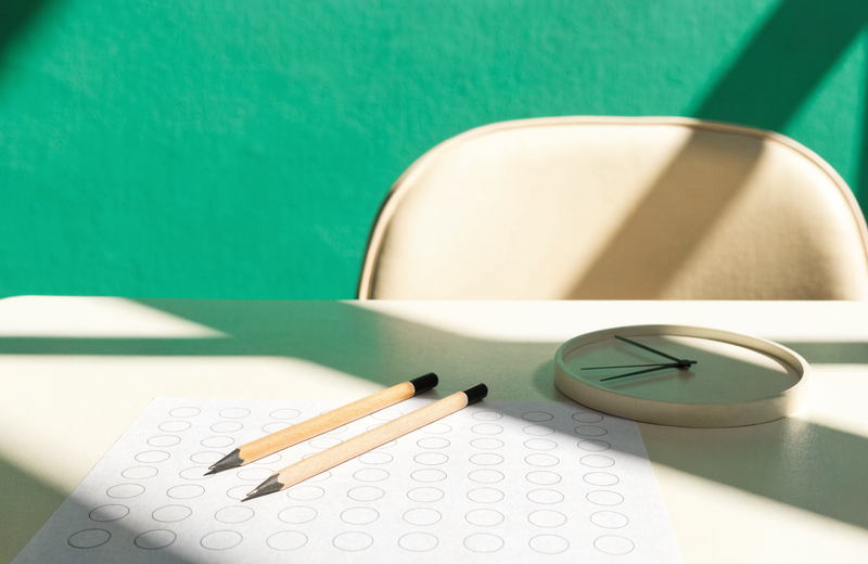 A clean exam desk with pencils, answer sheet + clock in focused morning light