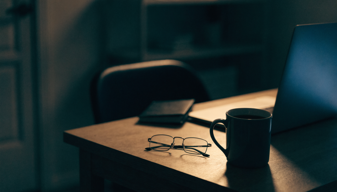 A home desk late at night lit by a low lamp, with a half-finished coffee and a notebook pushed aside