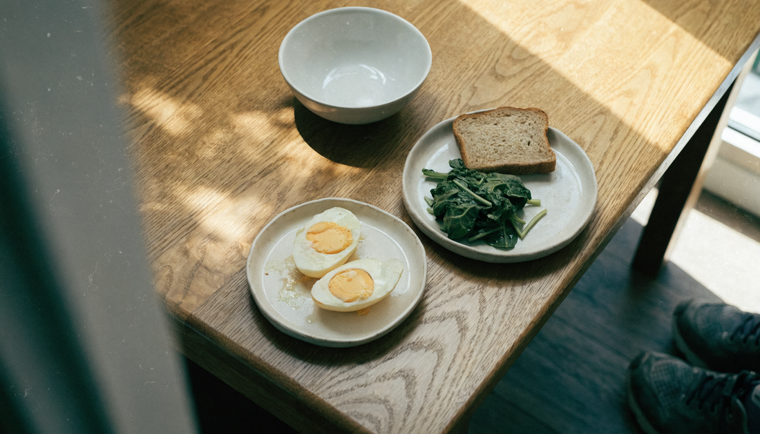 A plain breakfast of eggs, greens and whole grain toast on a warm oak table in morning daylight