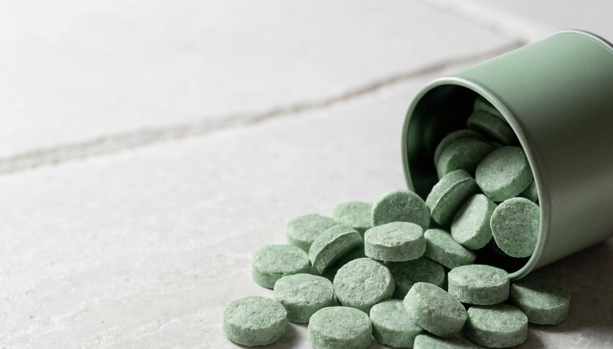 Focus mints scattered from a tipped green tin on light stone
