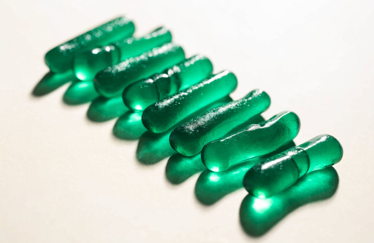 Translucent green energy gummies scattered across a cream studio background