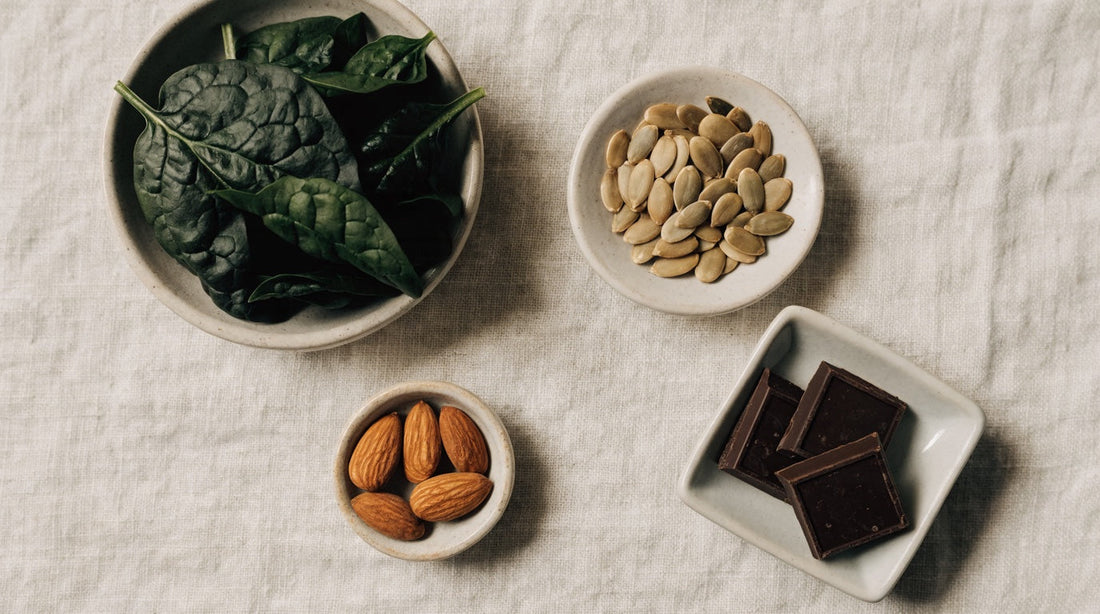 Magnesium-rich foods including spinach, pumpkin seeds, almonds and dark chocolate on linen